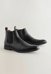 Botas Chelsea de cuero negro con paneles elásticos en los laterales, punta redondeada y tiradores; cuentan con una textura suave y acentos de tacón de madera.