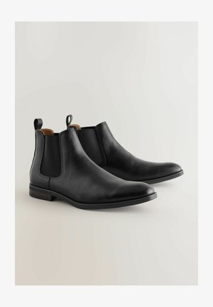 Bottes Chelsea noires en cuir avec des panneaux latéraux élastiques, bout arrondi et tirants; présentent une texture lisse et des accents de talon en bois.