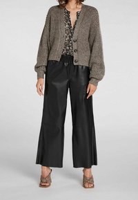 Gebreide cardigan in bruin met een geribbelde textuur, gecombineerd met zwarte leren wijde broek met een ontspannen pasvorm en zijsplitten, en taupe hakken.