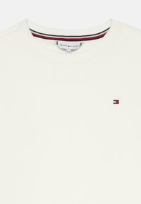 Hvid crewneck skjorte med Tommy Hilfiger-logo broderet på brystet og rød, hvid og blå stribet detalje indeni kraven.