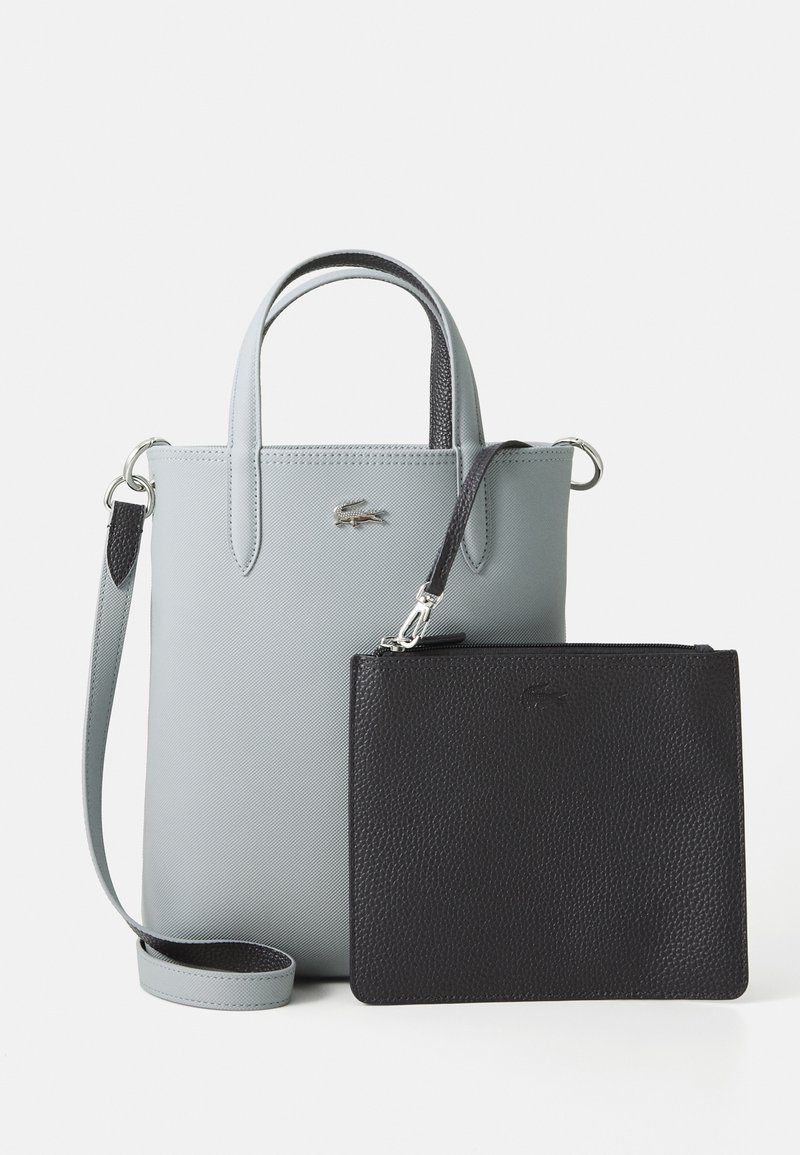 Light gray tote bag with double handles and shoulder strap, accompanied by a smaller textured black pouch with zipper and wrist strap.