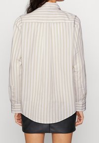 Beige und weiß gestreiftes Langarmshirt mit Knopfmanschette und abgerundetem Saum, das einen lässigen Schnitt und eine weiche Baumwollähnliche Textur aufweist.
