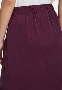 Une jupe bordeaux avec une taille élastique, présentant une texture lisse et un design ample s'étendant jusqu'à la cheville.