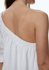 Top blanc décolleté avec un col froncé et des manches amples. Tissu doux et léger avec une texture lisse.
