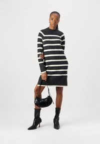 Robe rayée en tricot noir et crème, avec une texture côtelée, des manches longues et un ourlet au-dessus du genou ; associée à un sac à main noir.