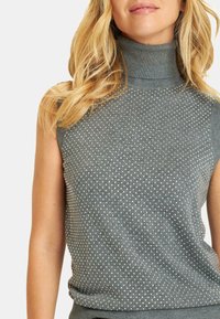 Suéter sin mangas de punto gris con un patrón texturizado que presenta pequeños puntos plateados por toda la prenda. Tejido suave con una silueta ajustada.