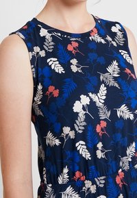 Sukienka bez rękawów, w granatowej bazie z floralnym wzorem w czerwonym, niebieskim i białym kolorze. Miękka tkanina z dopasowanym wcięciem w talii i okrągłym dekoltem.