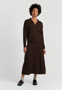 Ensemble en tricot marron en deux pièces comprenant un haut à manches longues de style polo avec un col en V et une jupe assortie arrivant aux chevilles. Texture lisse.