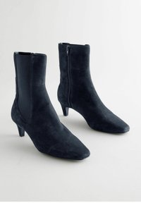 Bottines bleu marine en daim doux avec un bout pointu et un petit talon. Comprend des panneaux latéraux élastiques et une fermeture éclair sur le côté pour un enfilement facile.