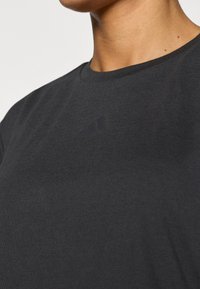 Μαύρο βαμβακερό t-shirt με στρογγυλή λαιμόκοψη και μικρό, αδιαφανές λογότυπο στο στήθος. Το ύφασμα έχει λεία υφή.