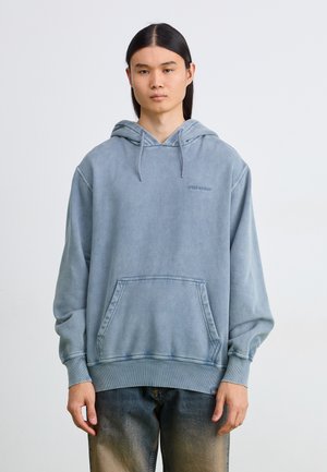 Sudadera con capucha de color azul claro, con un bolsillo frontal, corte holgado y puños de canalé. Presenta un logo sutil en el pecho y una textura suave.
