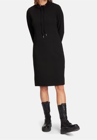 Svart hoodieklänning med ribbad textur, dragsko i halsen och rak skärning, kombinerad med knähöga svarta snörstövlar.