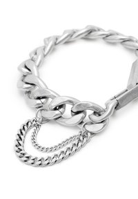 Bracelet en chaîne métallique argentée avec des maillons interconnectés et un design superposé, comportant un pendentif en chaîne plus petite attaché. Fini brillant.