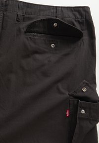 Black pants featuring a smooth fabric, angled side pockets with snap closures, and a small red Levi's tag on the right pocket.