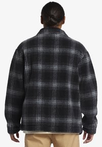 Black and gray plaid fleece jacket, featuring a textured surface, wide collar, and loose fit. Long sleeves with cuffed hems.