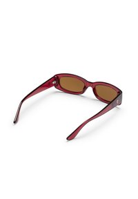 Κόκκινα διαφανή ορθογώνια γυαλιά ηλίου με καφέ φακούς που ακουμπούν ανοιχτά σε μια λευκή επιφάνεια.