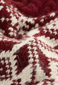 Strickstoff in Burgunderrot und Creme mit einem geometrischen Muster. Die Textur wirkt weich und flauschig mit sichtbaren Fasern und einer dicken Webart.