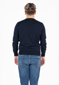 Temno modra pletena jopica z dolgimi rokavi in ribastimi manšetami, v kombinaciji z zbledelimi modrimi jeans hlačami z zadnjimi žepi.