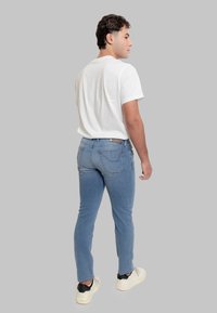 Jeans azzurri chiaro a taglio aderente, con cinque tasche e dettagli di cuciture sottili, abbinati a una t-shirt bianca semplice e sneakers nere.