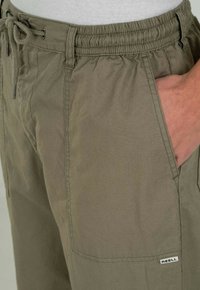 Khakihosen mit elastischem Bund, Kordelzug, Seitentaschen und einem kleinen Markenlabel. Der Stoff wirkt glatt und leicht.