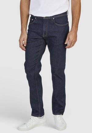 Blauwe spijkerbroek met een recht gesneden pasvorm, voorzien van oranje stiksels, voorzakken en een klassieke knoopsluiting. Gepaarde met witte sneakers.