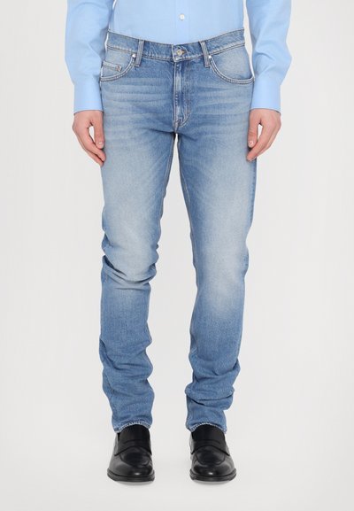 Jean slim bleu clair avec décoloration, design à cinq poches, couture traditionnelle et bas retroussés, associés à une chemise bleu clair à boutons.