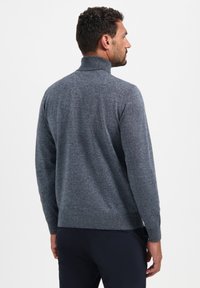Grijze gebreide trui met hoge kraag, lange mouwen en geribde manchetten en onderkant. Zachte textuur met een subtiel gemêleerd patroon, gedragen door een man van achteren.