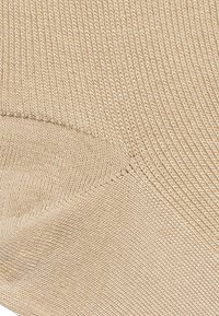 Beżowa skarpeta w prążki charakteryzująca się gładką teksturą i zwężającym się kształtem. Tkanina ma drobne przeszycia wzdłuż krawędzi oraz dzianinowy wzór na całej powierzchni.