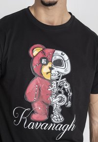 Camiseta negra con un gráfico de un oso dividido por la mitad: un lado rojo con costuras, el otro metálico con características robóticas. El texto dice "Kavanagh".