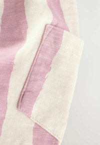 Tissu en coton avec des rayures roses et blanches, comportant une poche plaquée. La texture semble douce et les coutures sont visibles le long des bords.