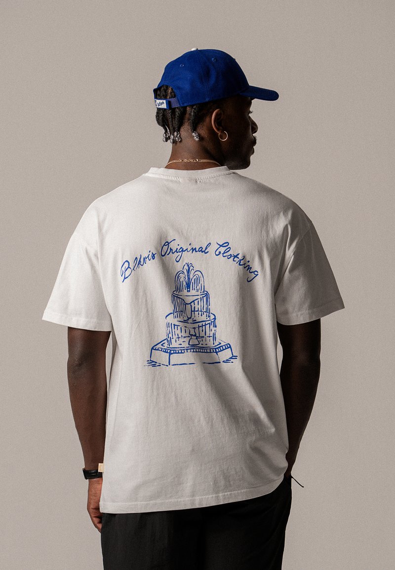 Balts T-krekls ar zilu grafiku, kurā attēlots strūklaka, un ar tekstu "Blerk's Original Clothing" izliekta stilā uz muguras.