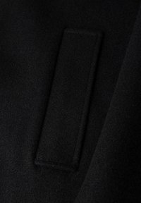 Schwarzer Wollstoff mit einem rechteckigen Patch. Die Textur ist glatt und dicht, mit einem leichten Glanz im Licht. Einfaches, minimalistisches Design.