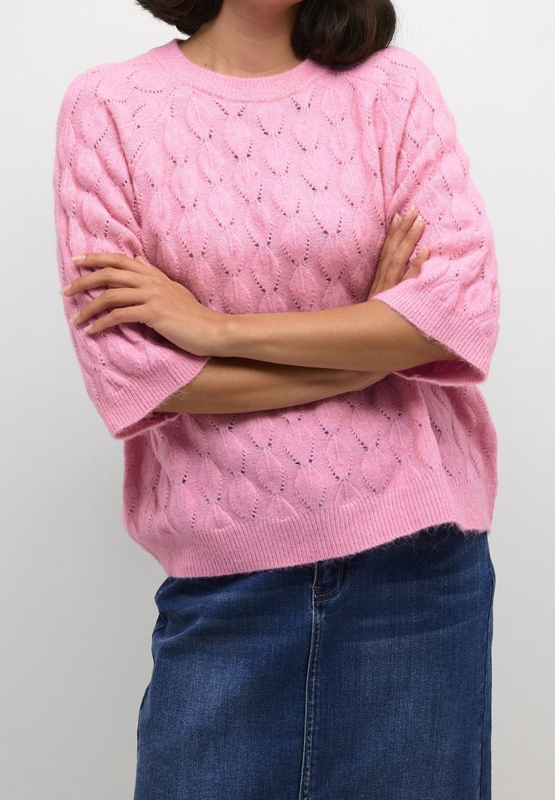 Rosa gestrickter Pullover mit Blattmuster, kurzen Ärmeln und geripptem Ausschnitt. Wird über einem Jeansrock getragen und hat eine lockere Passform.