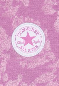 Logo patch Converse All Star Chuck Taylor in rosa su sfondo di tessuto rosa chiaro texture.