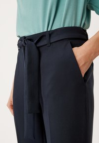 Navyblauwe op maat gemaakte broek met een gladde textuur, voorzien van een bijpassende stoffen riem en zijzakken, gestyled met een lichtblauw topje.