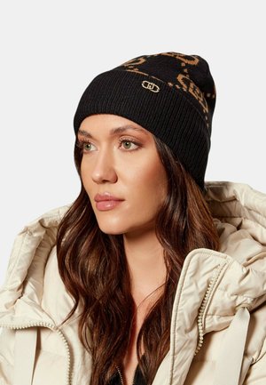 Black knit beanie with tan patterned design and gold logo accent. Features ribbed texture and close-fitting shape.