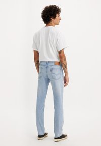 Lys blå denimjeans med rett benpassform, med baklommer og en lærpatch. Kombinert med en hvit kortermet skjorte.