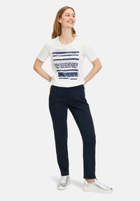 White short-sleeve t-shirt with navy graphic stripes, paired with navy slim-fit pants and silver sneakers. Simple, casual, and versatile look.