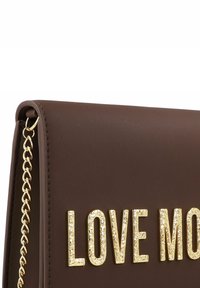 Dunkelbraune Lederhandtasche mit goldener Kettenriemen und erhabenen, goldfarbenen, strukturierten Buchstaben, die "LOVE MO" buchstabieren.