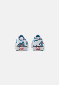 Baskets blanches en toile avec des motifs géométriques colorés en bleu et rose, semelles en caoutchouc blanches et logo Vans rouge sur le talon.