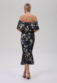 Sininen off-shoulder-mekko kultaisella kukkakuviolla, vartalonmyötäinen siluetti, levenevä helma ja vetoketj closure takana. Korkeakorkoiset beige kengät.