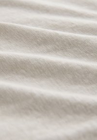 Tissu doux beige clair avec un motif subtil de tissage diagonal et des plis légers créant une surface texturée et confortable.