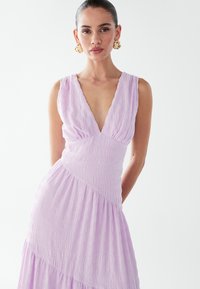 V-neck lavender dress with a textured, crinkled fabric, featuring a fitted waist and layered skirt. Simple, elegant silhouette.