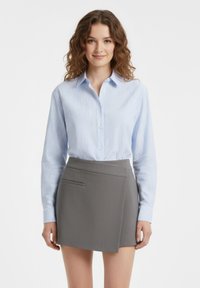 Camicia a righe azzurro chiaro con bottoni e maniche lunghe abbinata a una gonna a portafoglio grigia con tasca laterale e tessuto strutturato.