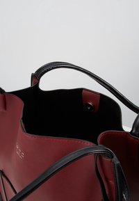 Borsa tote rossa in pelle con manici neri, interno in materiale scamosciato nero, presenta una chiusura a scatto magnetico e un dettaglio del logo impresso.