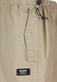 Shorts beiges en tissu léger, dotés d'une taille élastique, d'un cordon de serrage réglable et d'une poche latérale avec une étiquette logo.