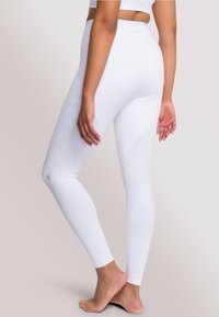 Leggings bianchi a coste con vita alta e design senza cuciture. Presentano un branding minimale e una silhouette aderente.