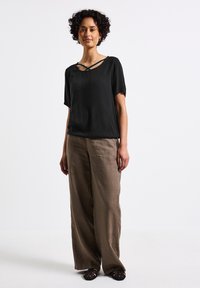Top nero a maniche corte con scollatura incrociata, abbinato a pantaloni lunghi in lino beige chiaro e scarpe mocassino nere intrecciate.