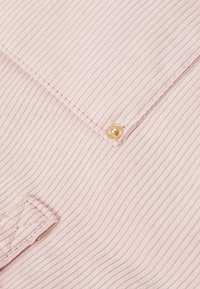 Tissu côtelé rose clair avec une surface texturée, présentant un bouton doré et des détails cousus, mettant en valeur un design à rabat et une sensation douce.