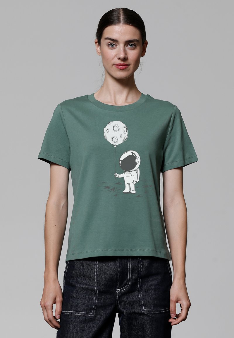 Groene katoenen T-shirt met een witte astronautafbeelding die een maanvormige ballon vasthoudt. Korte mouwen en een ontspannen pasvorm.